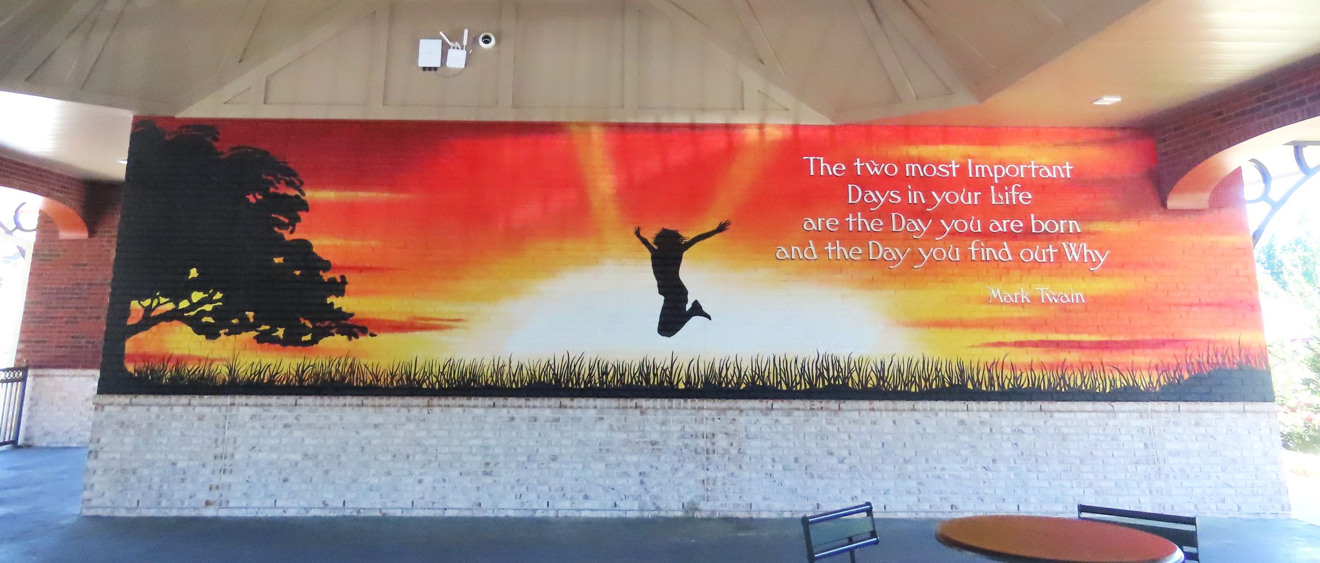 Mural of sunset with silhouette of woman jumping and Mark Twain Quote