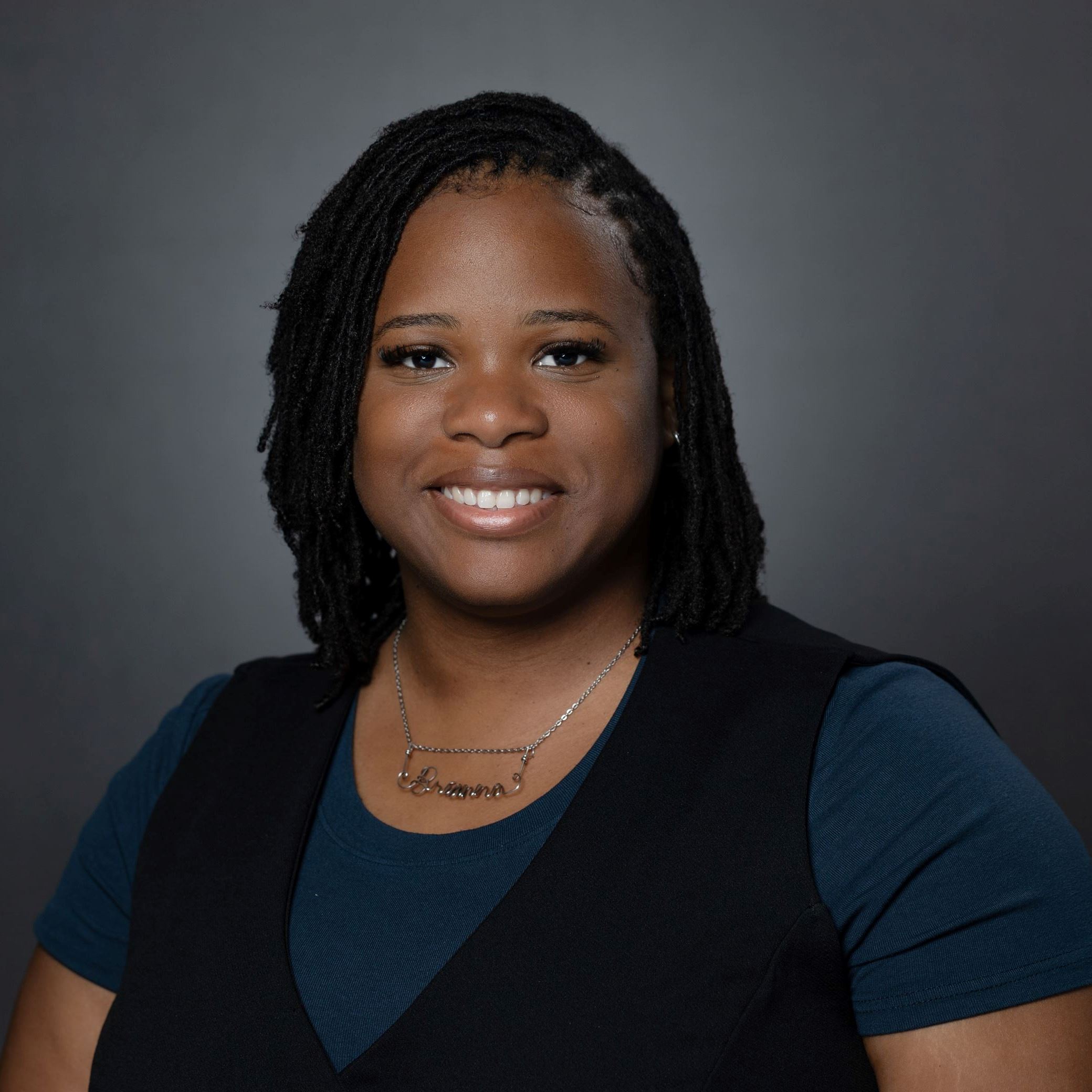 Headshot of Brianna Bower - Female with chin length hair wearing black vest over blue shirt