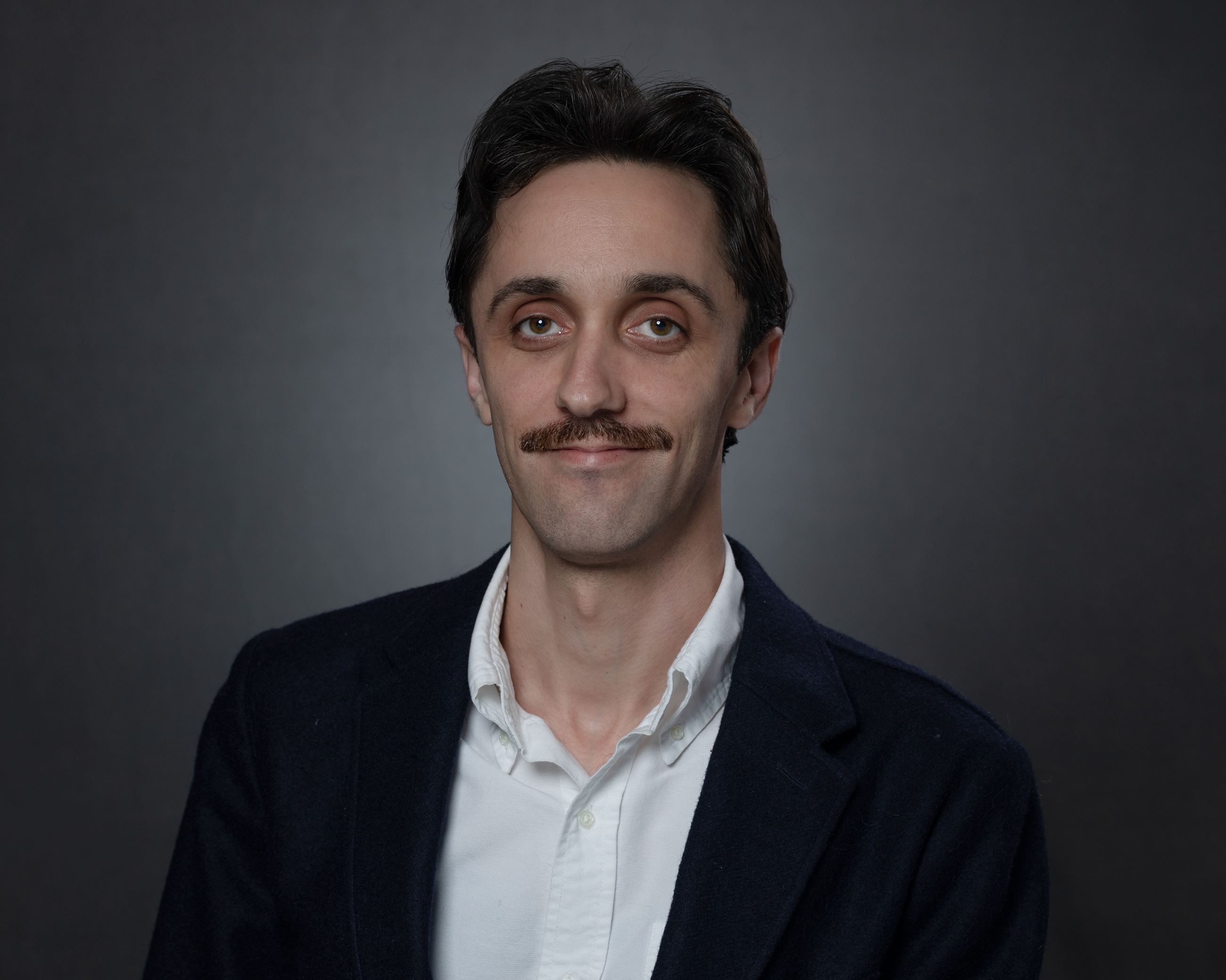 Headshot of Reid Turner male with short brown hair and mustache wearing black blazer