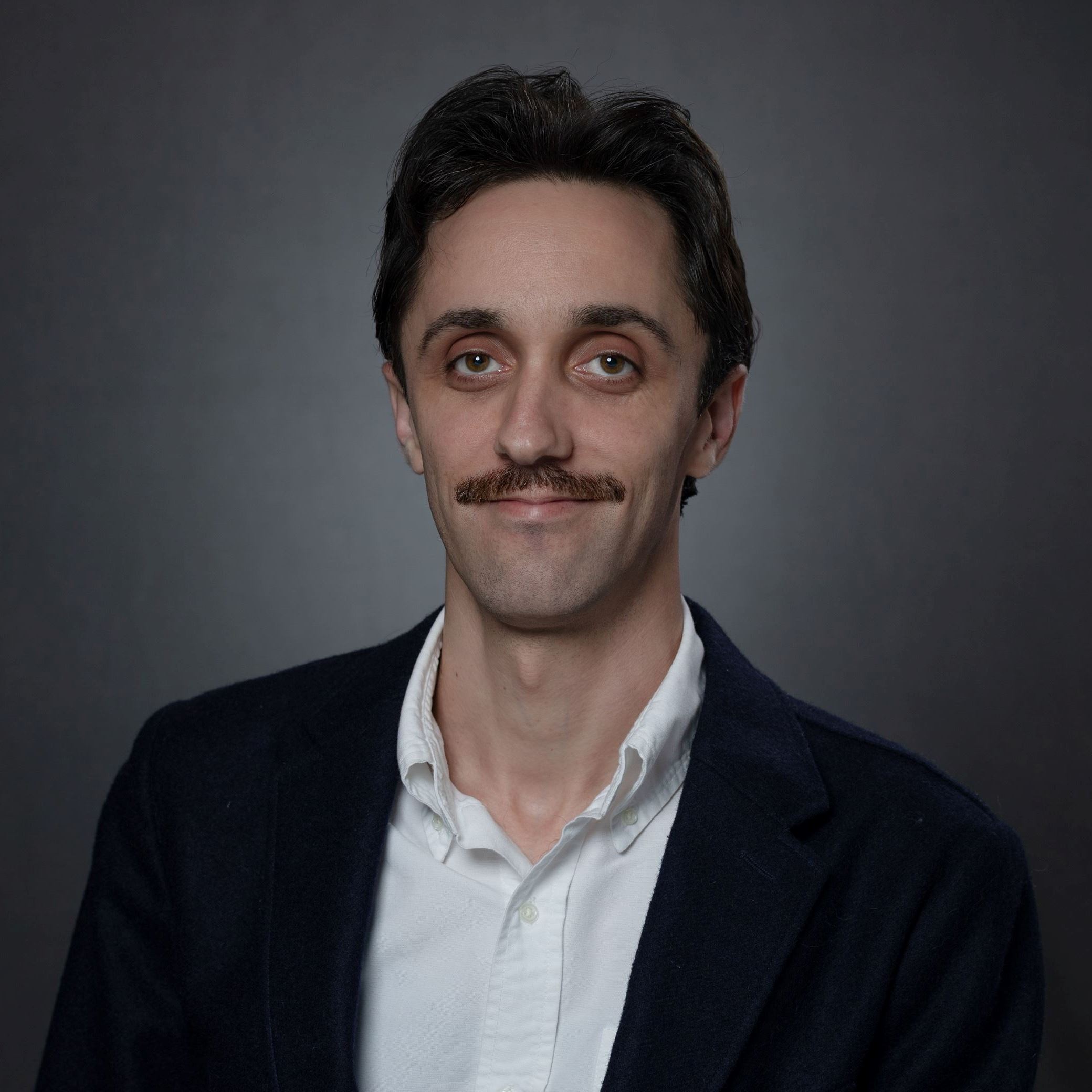 Headshot of Reid Turner male with short brown hair and mustache wearing black blazer