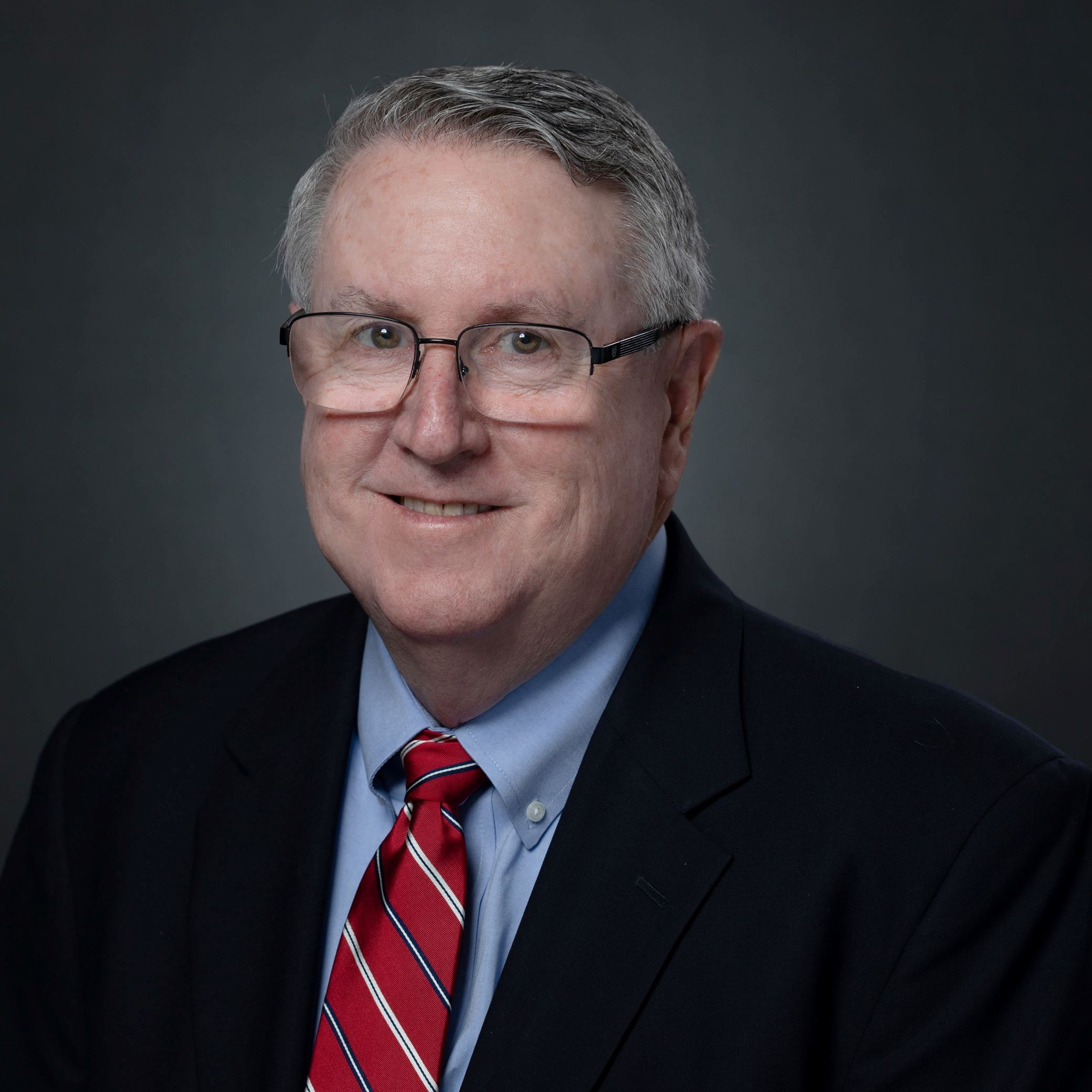 Headshots of Roy Whitehead male with short gray hair and glasses wearing black suit