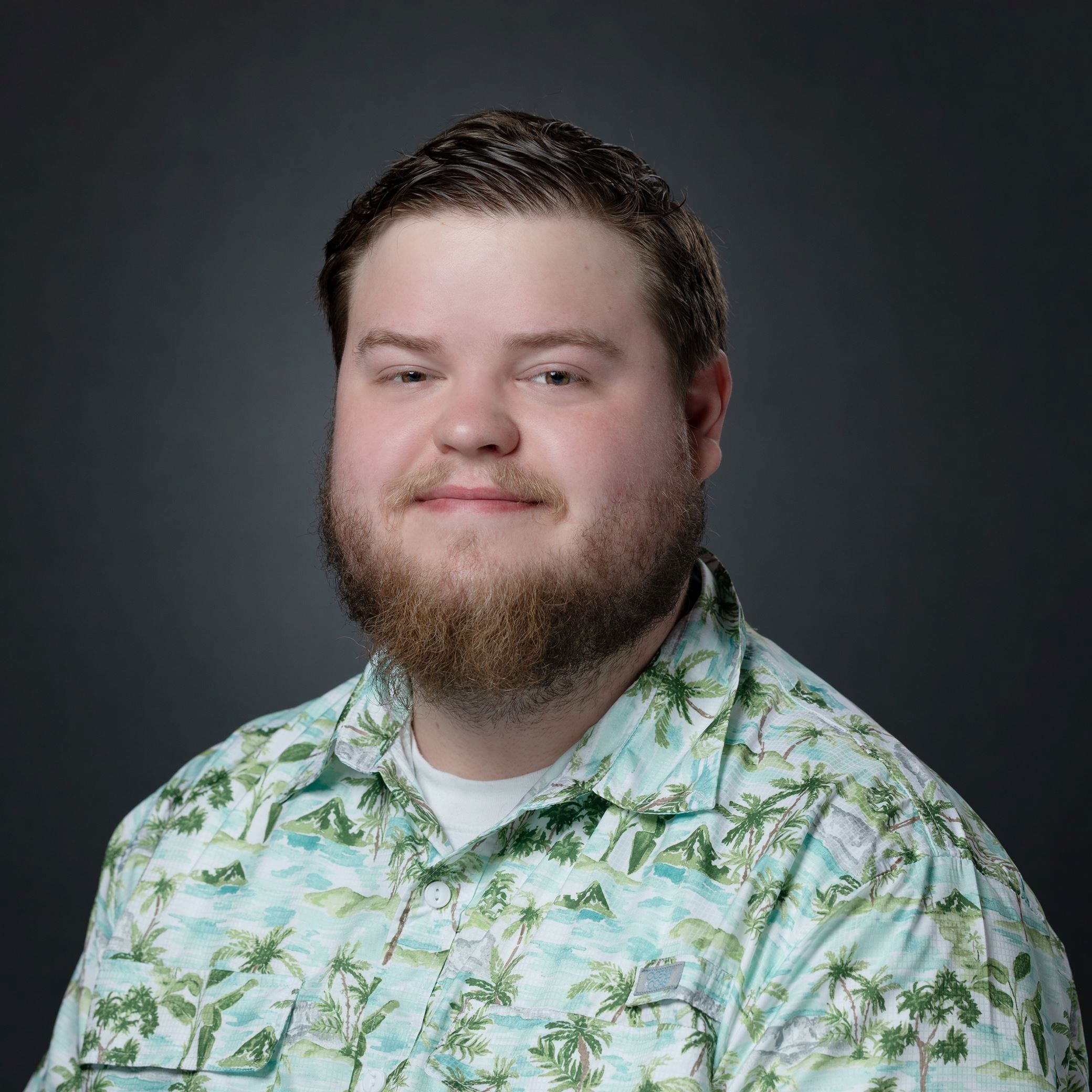 Headshot of Chad Mitchell male with brown hair/beard wearing tropical print collared shirt