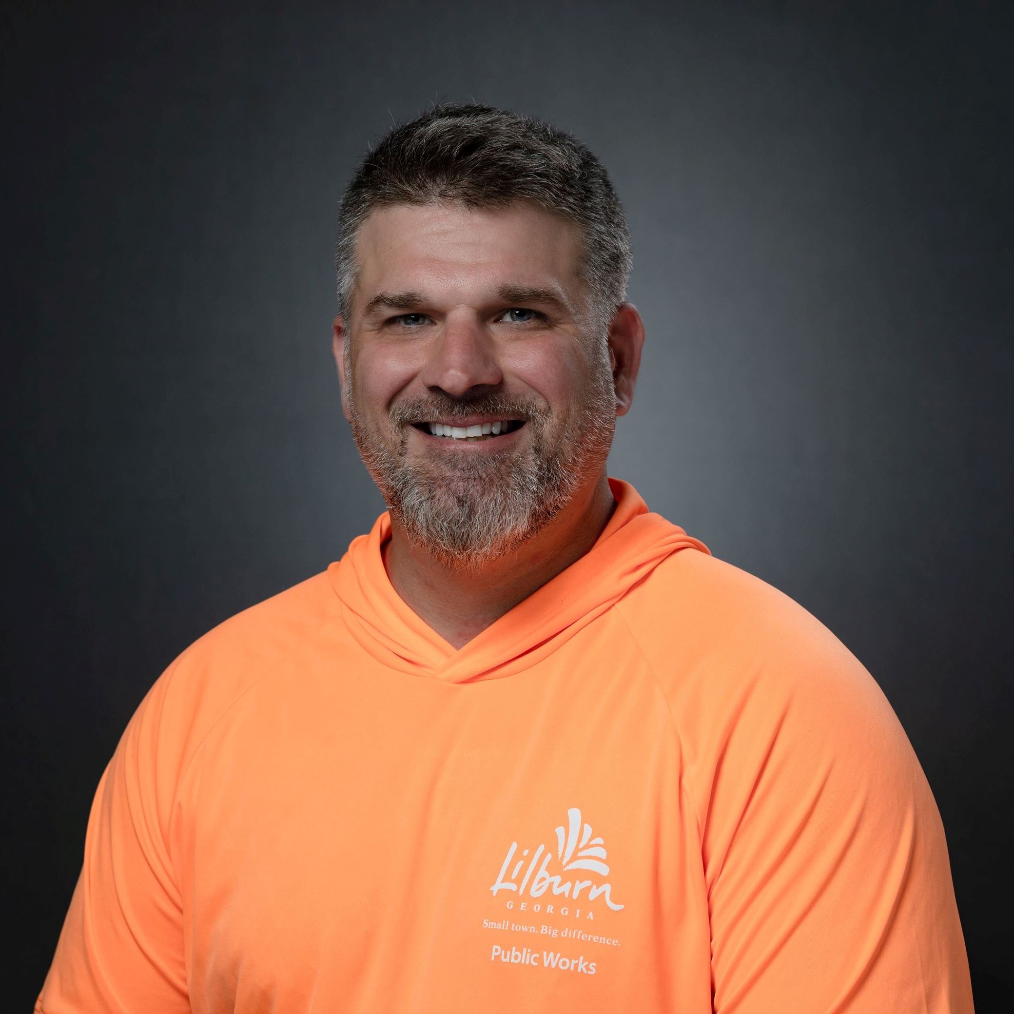 Headshot of Barrett Shaft male with salt and pepper hair/beard wearing orange polo shirt