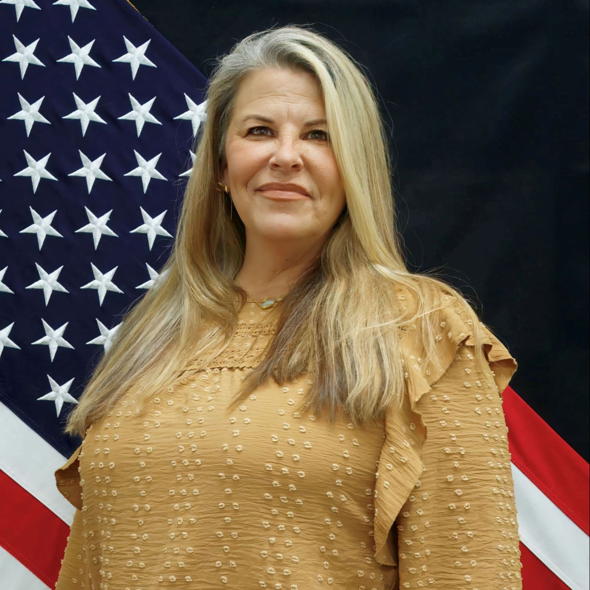 Headshot of Monica Sims female with long blonde hair wearing yellow long sleeve blouse